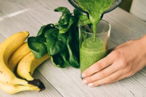 Female hand pours a smoothie of banana and spinach