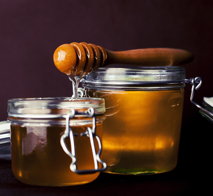Amber honey in a jar against a dark background.